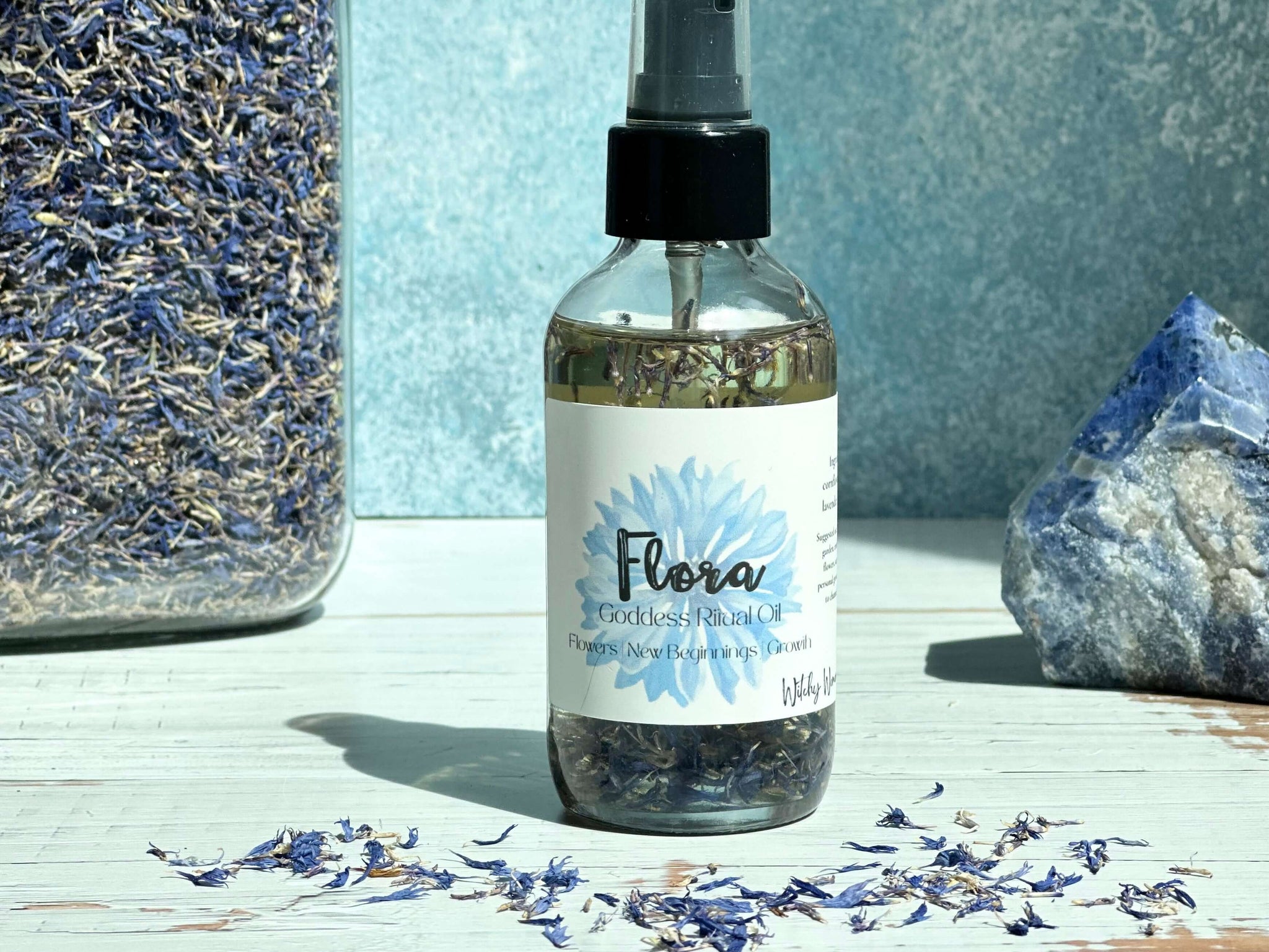 Bottle of Flora product with dried flowers and a crystal on a light surface.