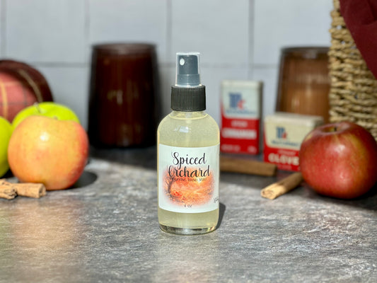 Spiced Orchard Purifying Hand Mist bottle on a countertop with apples and cinnamon sticks in the background.
