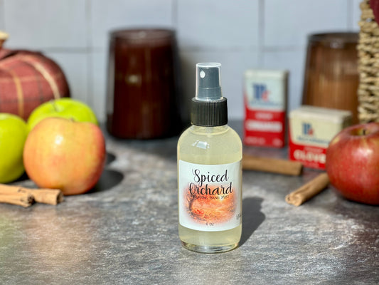 Spiced Orchard Purifying Hand Mist bottle on a countertop with apples and cinnamon sticks in the background.