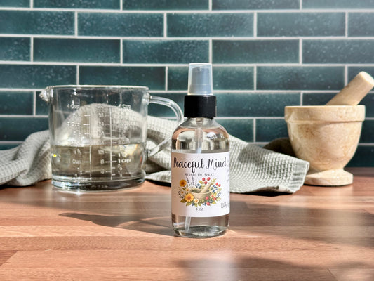 Bottle of Peaceful Mind essential oil spray on a wooden surface with a measuring cup and kitchen tools in the background.