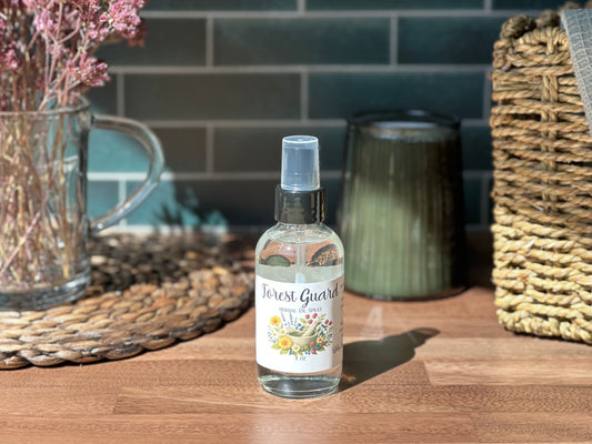 Bottle of 'Forest Guard' spray on a wooden surface with decorative items in the background.