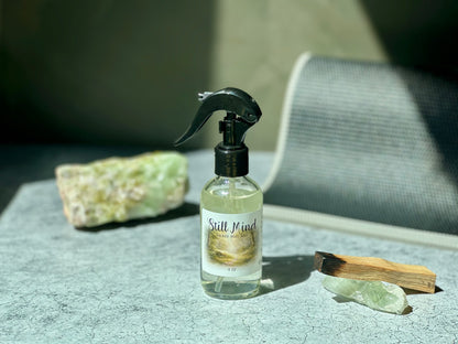 Still Mind Sacred Mat Mist bottle on a textured surface with crystals, promoting meditation and calmness.