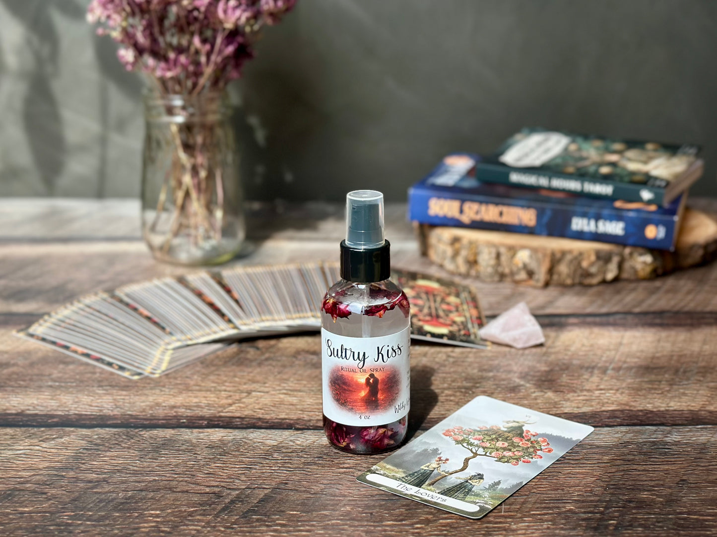 Sultry Kiss Ritual Oil Spray bottle with dried rose buds and tarot cards in a cozy setting.