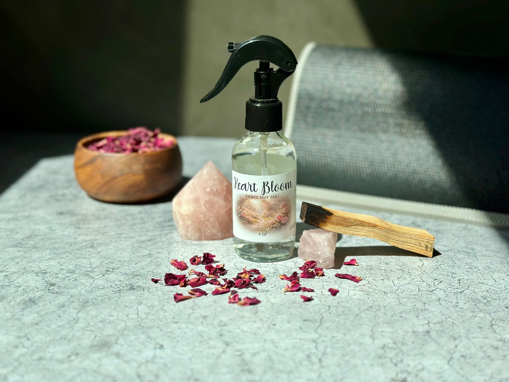 Heart Bloom Sacred Mat Mist bottle with pink crystals and dried rose petals on a textured surface.