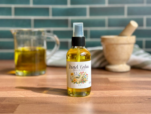 Bottle of 'Head Calm' herbal oil spray on a wooden table with kitchen items in the background.