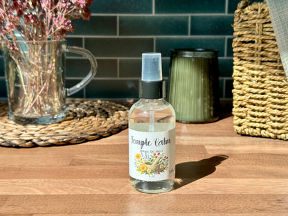 Temple Calm Herbal Oil Spray bottle on a wooden surface with a calming setting and natural light.