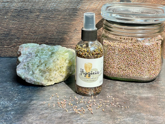 Healing ritual oil spray bottle beside a crystal and jar of seeds on a wooden surface.