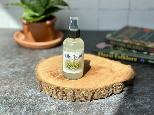 Bottle of Wild Earth Purifying Hand Mist displayed on a wooden surface with a background of plants and books.