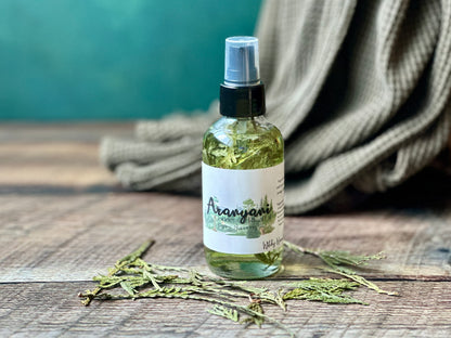 Bottle of Aranyani Goddess Ritual oil spray on a wooden surface with a green background