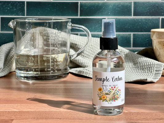 Bottle of Temple Calm spray next to a glass measuring cup on a wooden surface with a tiled wall background.