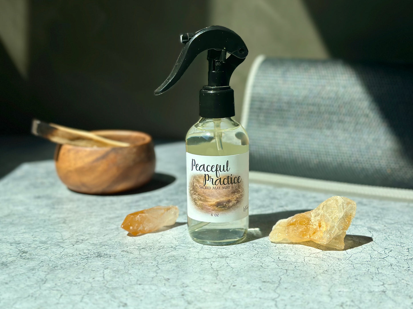Peaceful Practice Sacred Mat Mist spray bottle surrounded by crystals and a wooden bowl on a textured surface.
