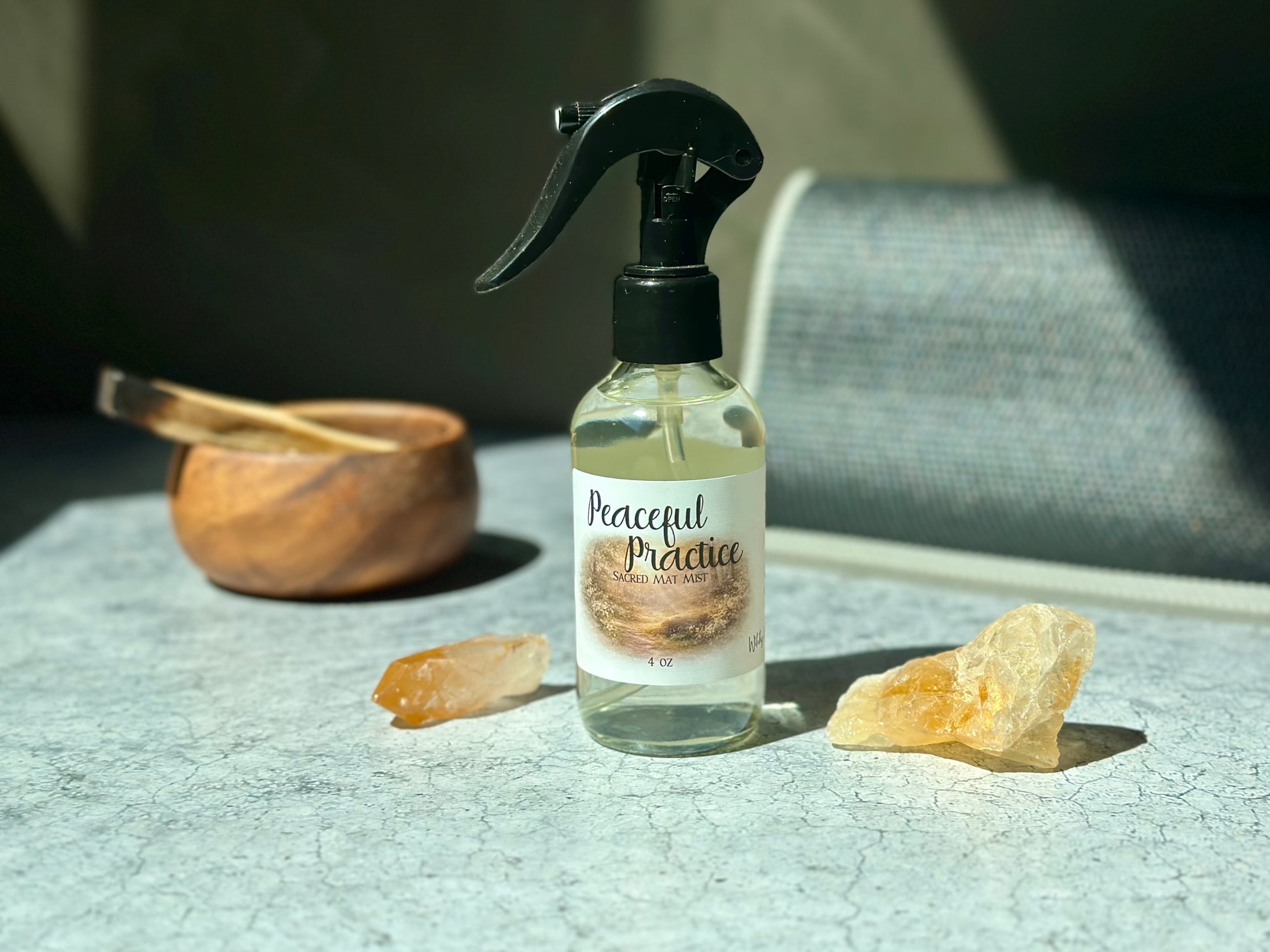 Peaceful Practice Sacred Mat Mist spray bottle surrounded by crystals and a wooden bowl on a textured surface.