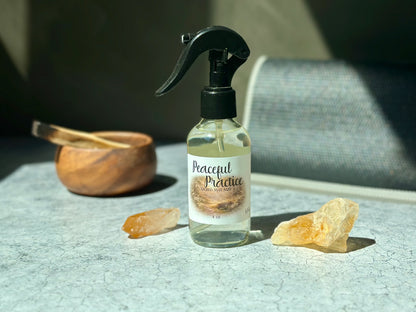 Peaceful Practice Sacred Mat Mist spray bottle surrounded by crystals and a wooden bowl on a textured surface.