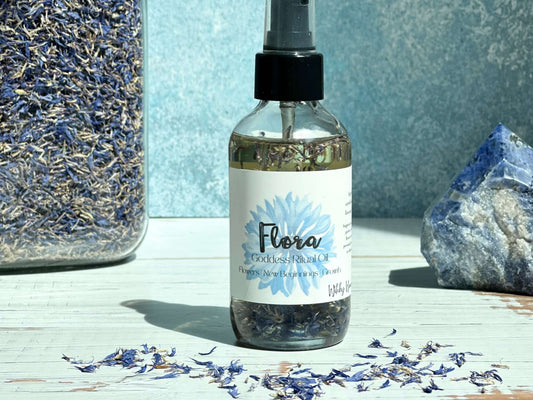 Flora Goddess Ritual Oil bottle surrounded by dried blue flowers and a gemstone.