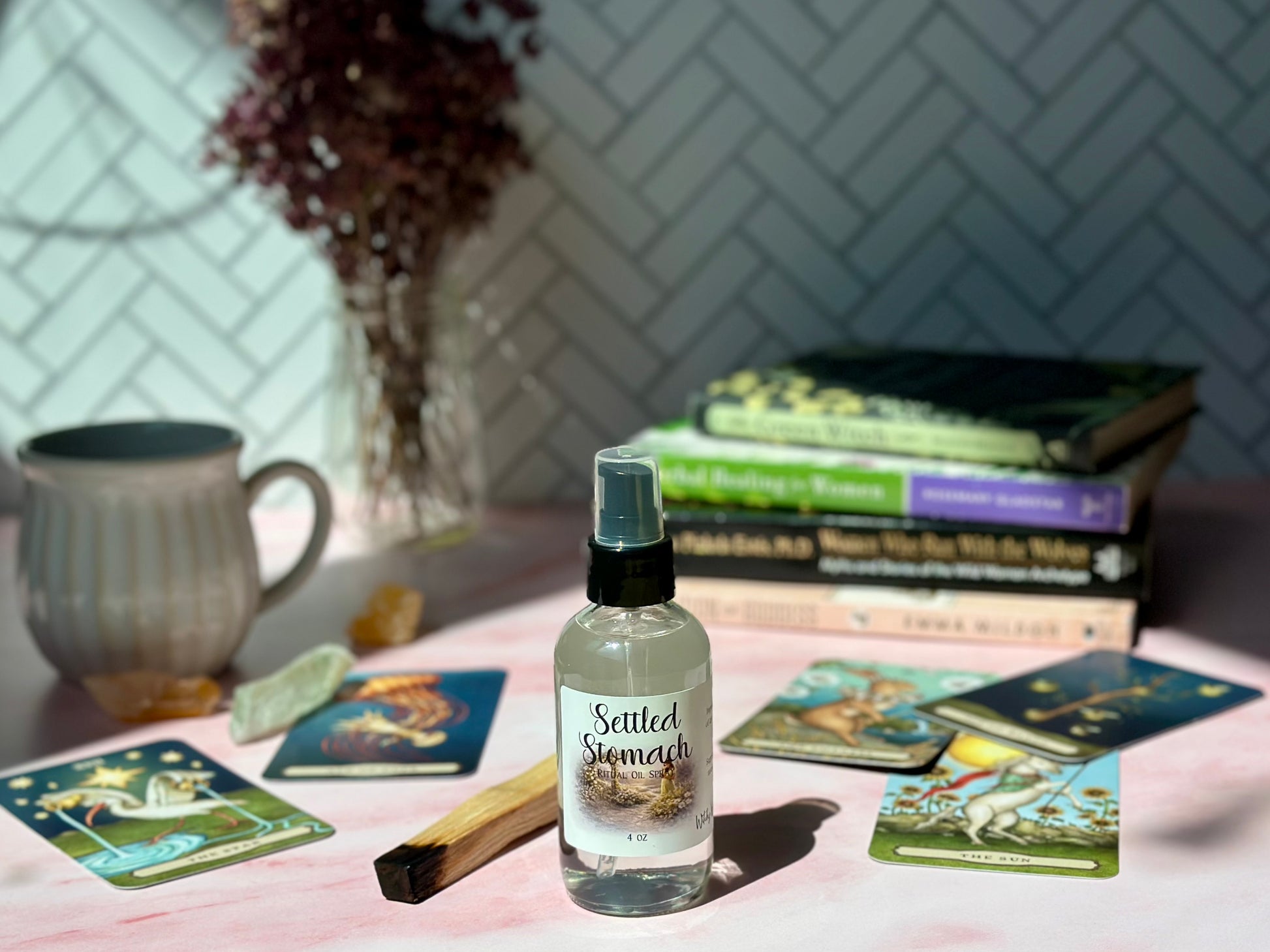 Settled Stomach Ritual Oil Spray bottle surrounded by books and tarot cards on a pink surface.