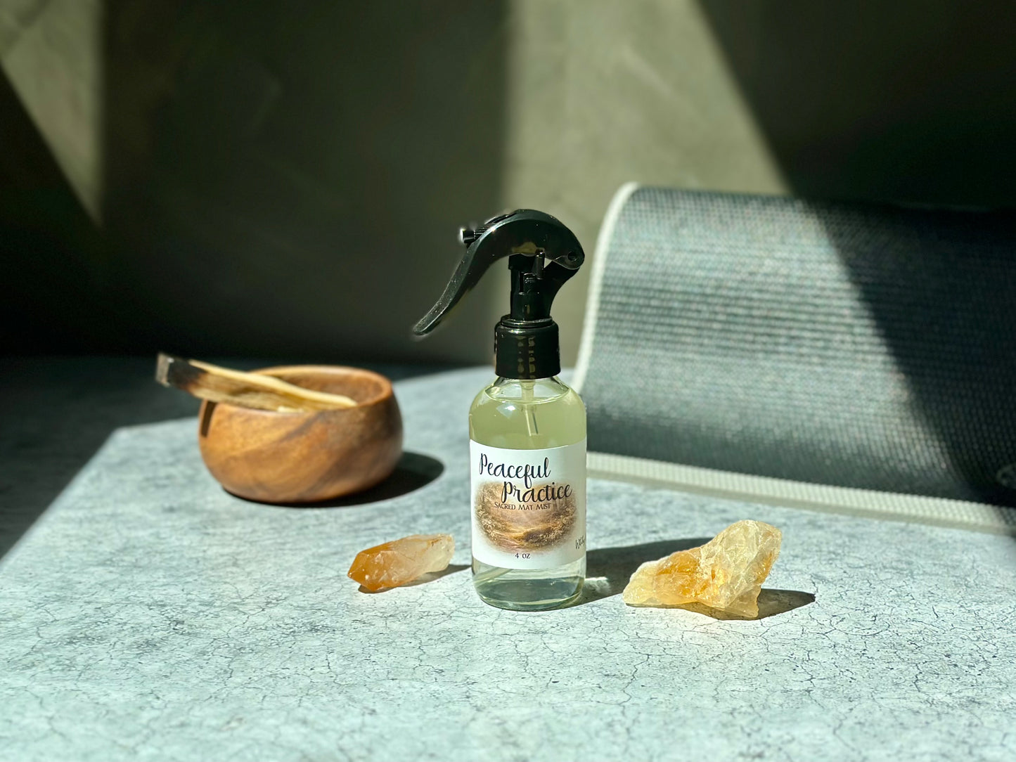 Peaceful Practice Sacred Mat Mist spray bottle surrounded by crystals and a wooden bowl on a textured surface.
