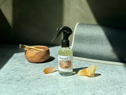 Peaceful Practice Sacred Mat Mist spray bottle surrounded by crystals and a wooden bowl on a textured surface.