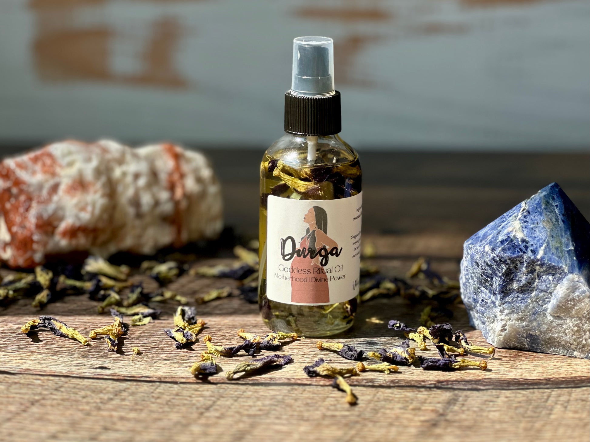 Durga Goddess Ritual Oil bottle surrounded by herbs and crystals on a wooden surface.