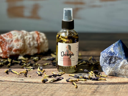 Durga Goddess Ritual Oil bottle surrounded by herbs and crystals on a wooden surface.