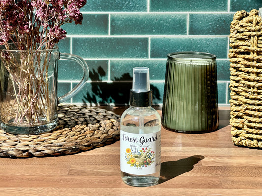 Bottle of 'Forest Guard' spray on a wooden surface with decorative items in the background.