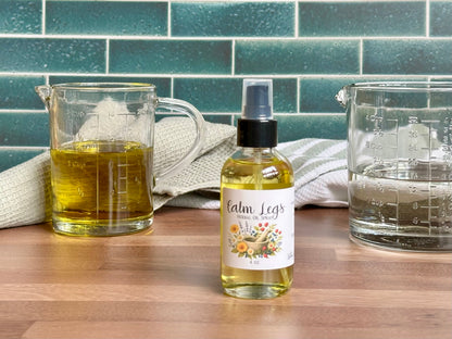 Bottle of 'Calm Legs' with two measuring cups on a wooden surface against a tiled wall.