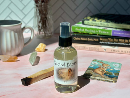 Sacred Breast Ritual Oil Spray bottle on a pink surface with books and crystals in a cozy setting.
