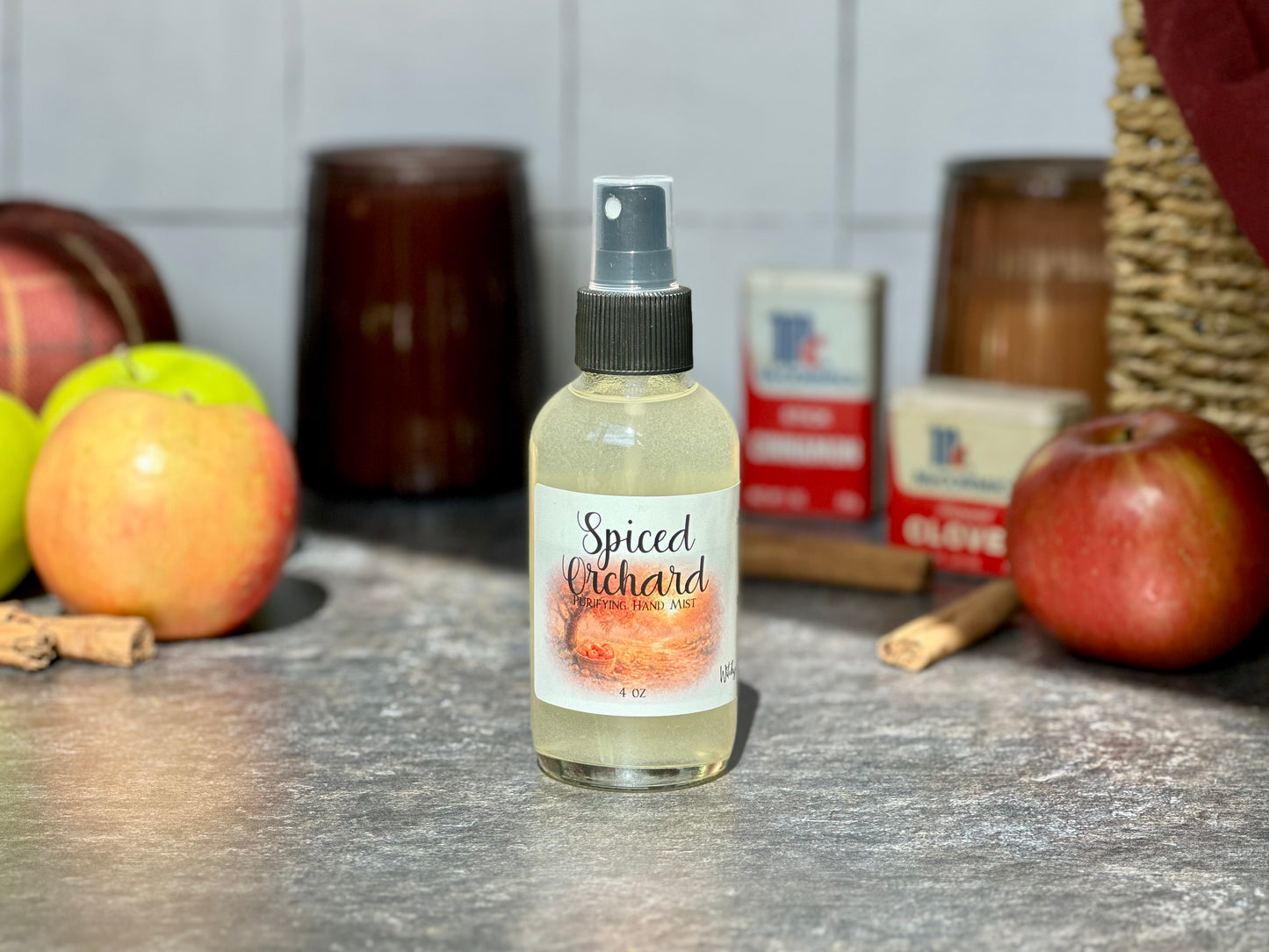 Spiced Orchard Purifying Hand Mist bottle on a countertop with apples and cinnamon sticks in the background.