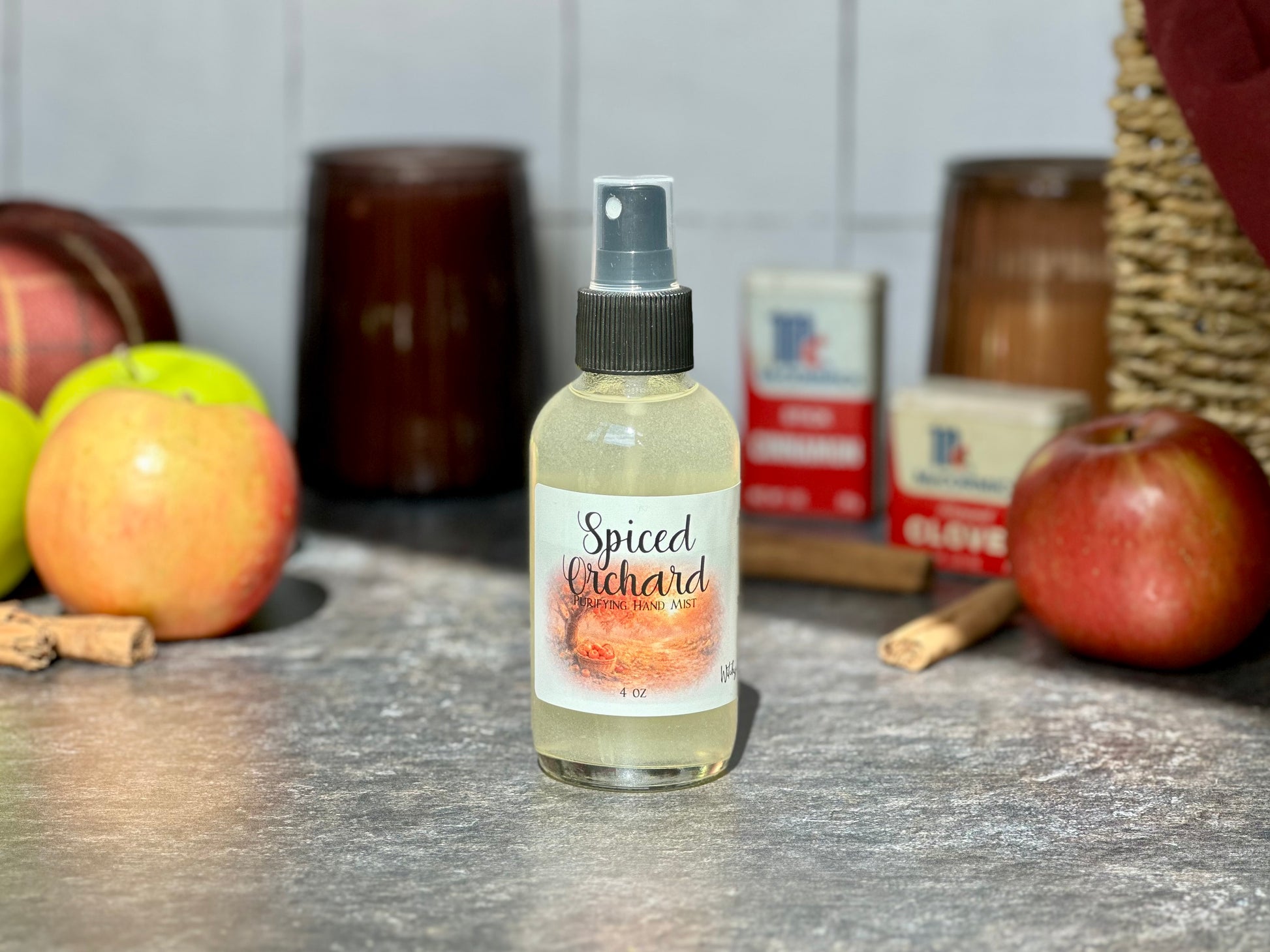 Spiced Orchard Purifying Hand Mist bottle on a countertop with apples and cinnamon sticks in the background.