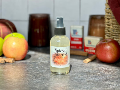 Spiced Orchard Purifying Hand Mist bottle on a countertop with apples and cinnamon sticks in the background.