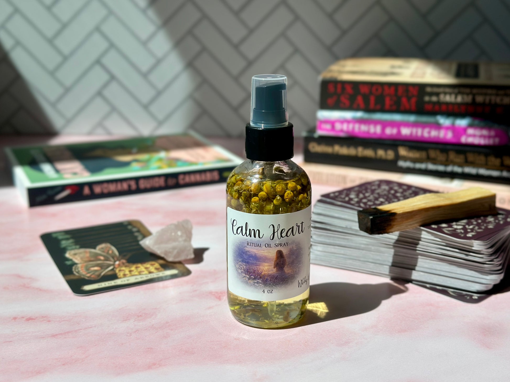 Calm Heart Ritual Oil Spray bottle on a pink surface with books and crystals in the background.
