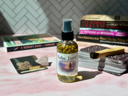 Calm Heart Ritual Oil Spray bottle on a pink surface with books and crystals in the background.