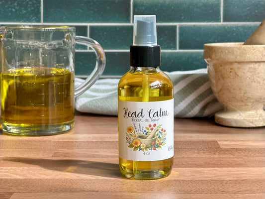 Bottle of 'Head Calm' herbal tincture on a wooden surface with a mug and mortar and pestle in the background.