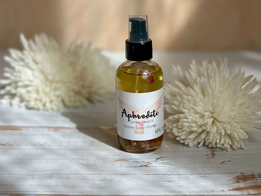 Aphrodite Goddess Ritual Oil bottle on a rustic wooden surface with decorative flowers in the background.