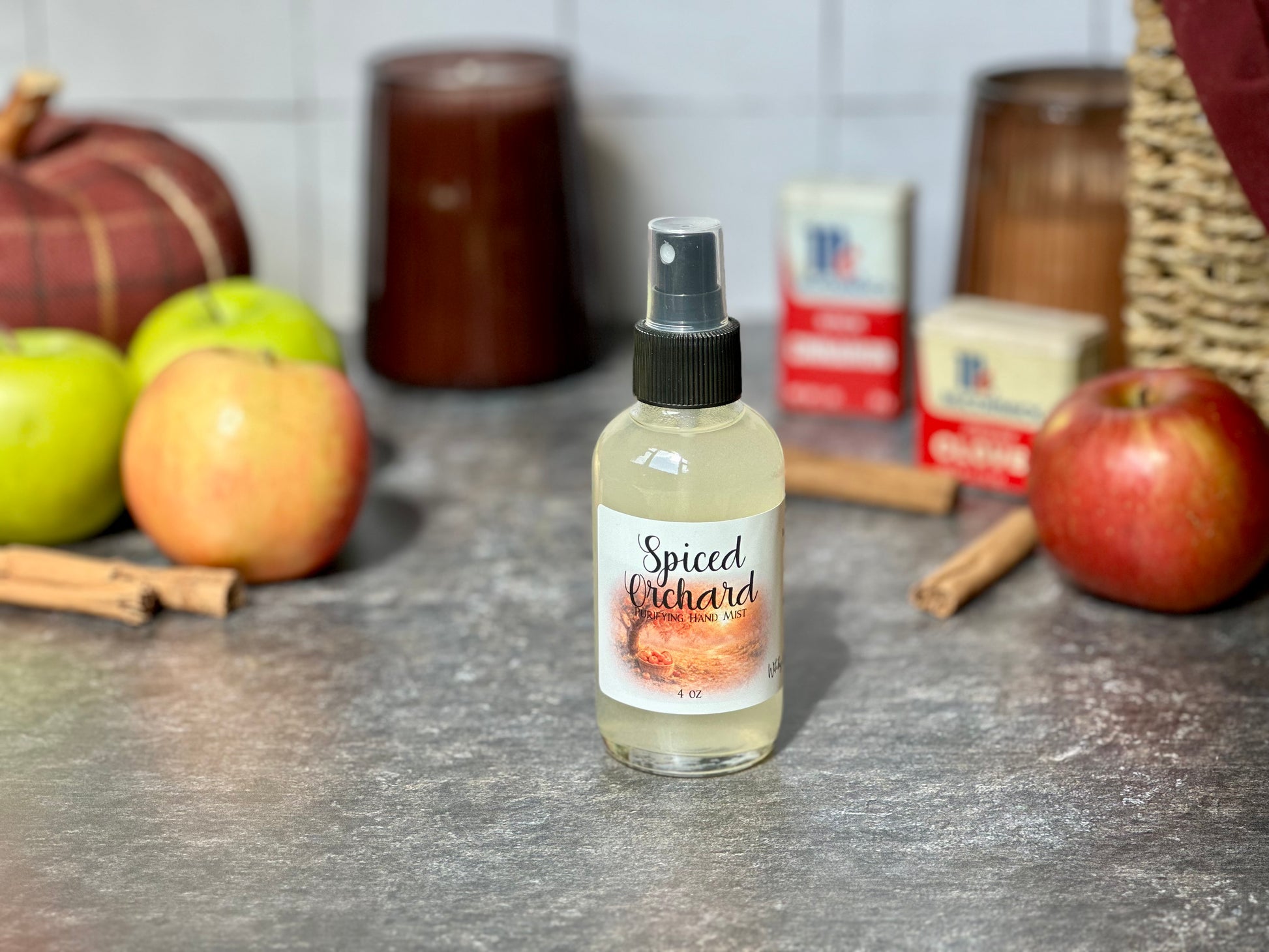 Spiced Orchard Purifying Hand Mist bottle on a countertop with apples and cinnamon sticks in the background.