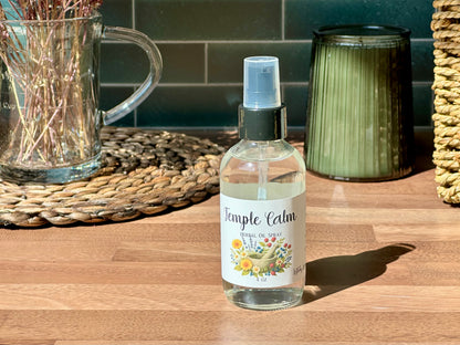 Temple Calm Herbal Oil Spray bottle on a wooden surface with a calming setting and natural light.