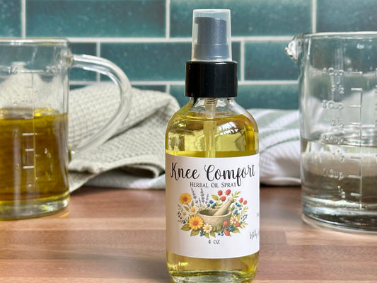 Bottle of 'Knee Comfort' herbal oil spray on a kitchen counter with glasses and a towel in the background.