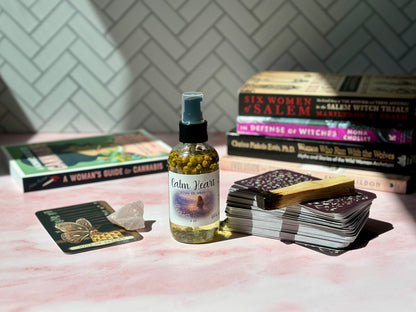 Calm Heart Ritual Oil Spray bottle on a pink surface with books and crystals in the background.