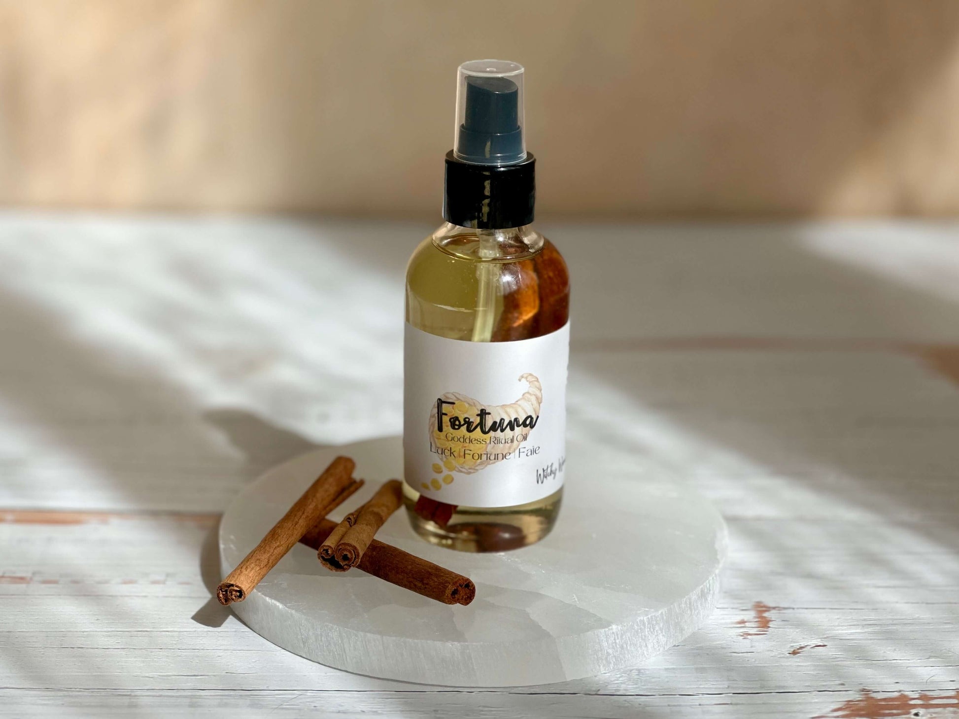 Fortuna Goddess Ritual Oil bottle with cinnamon sticks on a white circular stone surface.