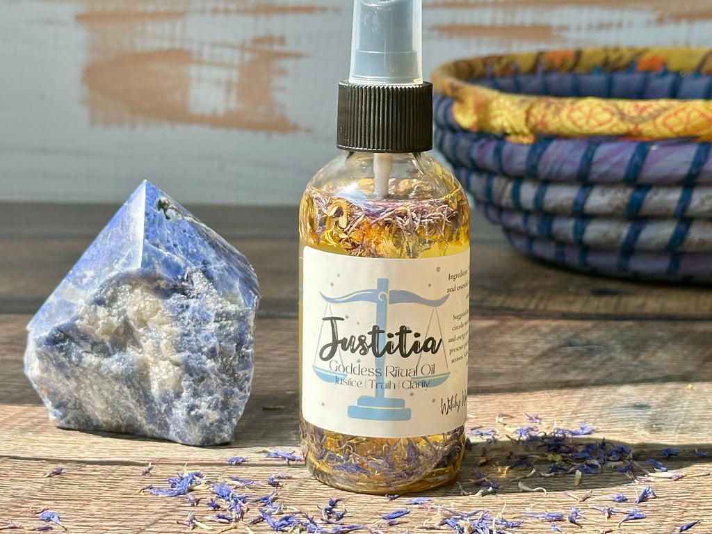 Bottle of 'Justitia' oil with a label, surrounded by lavender flowers and a crystal on a wooden surface.
