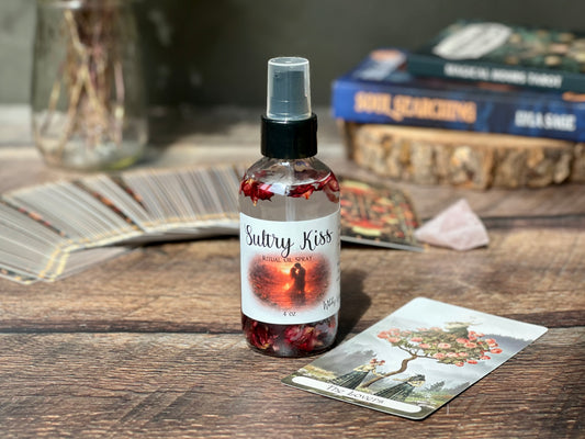 Sultry Kiss Ritual Oil Spray bottle with dried rose buds and tarot cards in a cozy setting.
