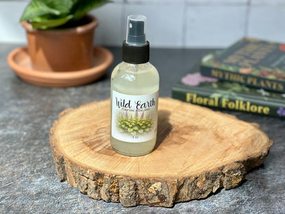Bottle of Wild Earth Purifying Hand Mist displayed on a wooden surface with a background of plants and books.