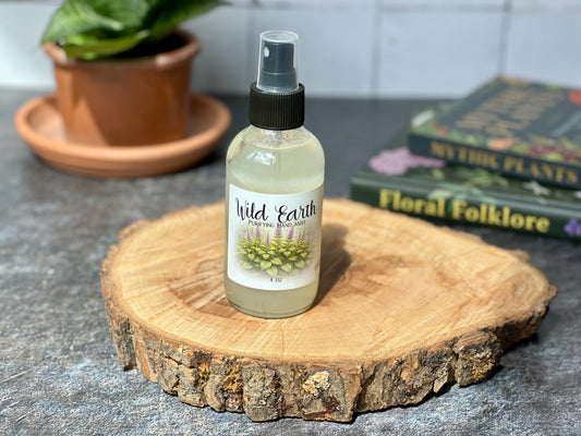 Bottle of Wild Earth Purifying Hand Mist displayed on a wooden surface with a background of plants and books.