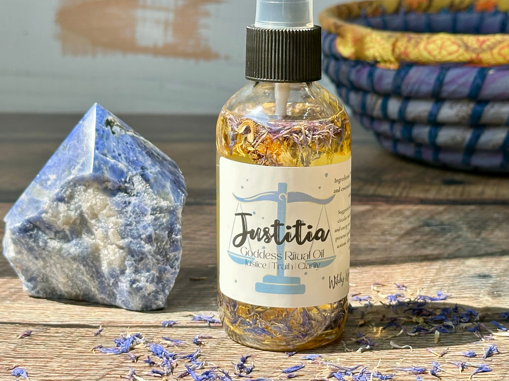 Bottle of 'Justitia' oil with a label, surrounded by lavender flowers and a crystal on a wooden surface.