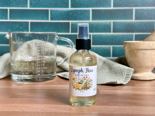 Bottle of Lymph Flow herbal oil spray on a wooden surface with a measuring cup and towel in the background.