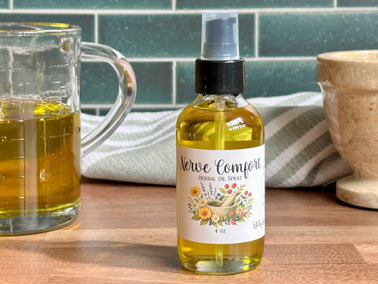 Bottle of 'Nerve Comfort' herbal oil spray on a wooden surface with a glass container and kitchen towel in the background.
