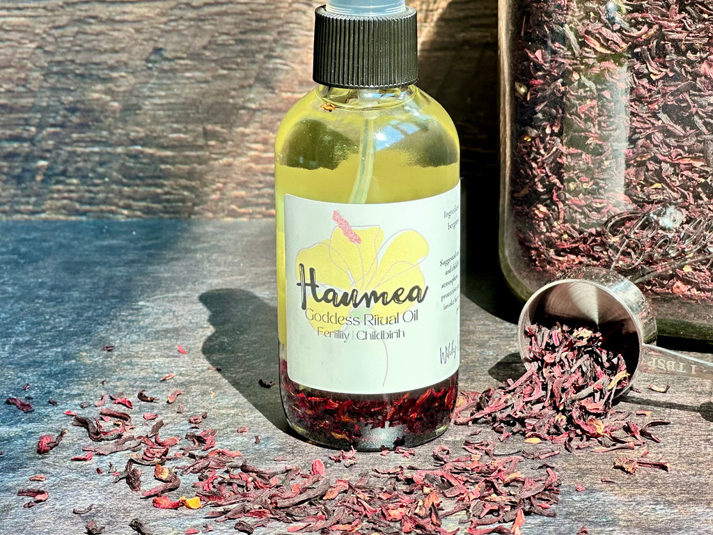 Bottle of Haumea Goddess Ritual Oil with dried hibiscus flowers on a wooden surface