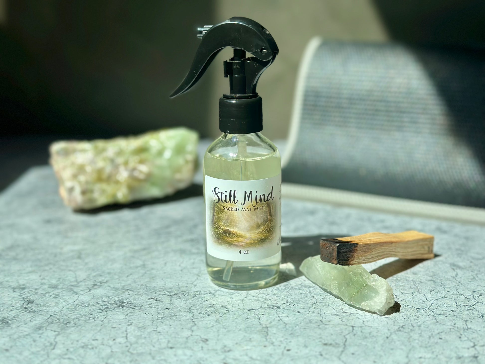 Still Mind Sacred Mat Mist bottle on a textured surface with crystals, promoting meditation and calmness.