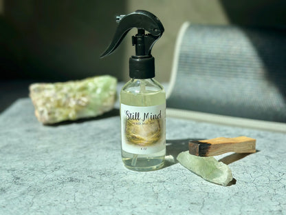 Still Mind Sacred Mat Mist bottle on a textured surface with crystals, promoting meditation and calmness.