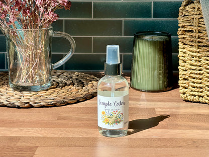 Temple Calm Herbal Oil Spray bottle on a wooden surface with a calming setting and natural light.