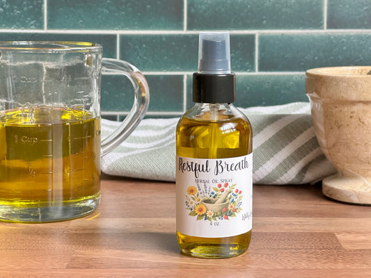 Bottle of 'Restful Breath' herbal spray on a wooden surface with a glass container and towel in the background.